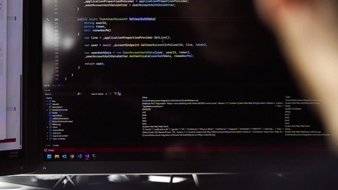 En person sidder foran en computer, der viser kode i et udviklingsmiljø, fokuseret på programmering og softwareudvikling.